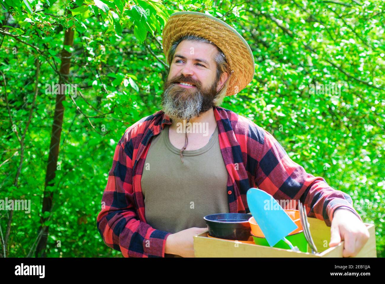 Homme heureux dans le jardin de printemps. Jardinier dans Eco Farm avec outils de jardinage de plantation Banque D'Images
