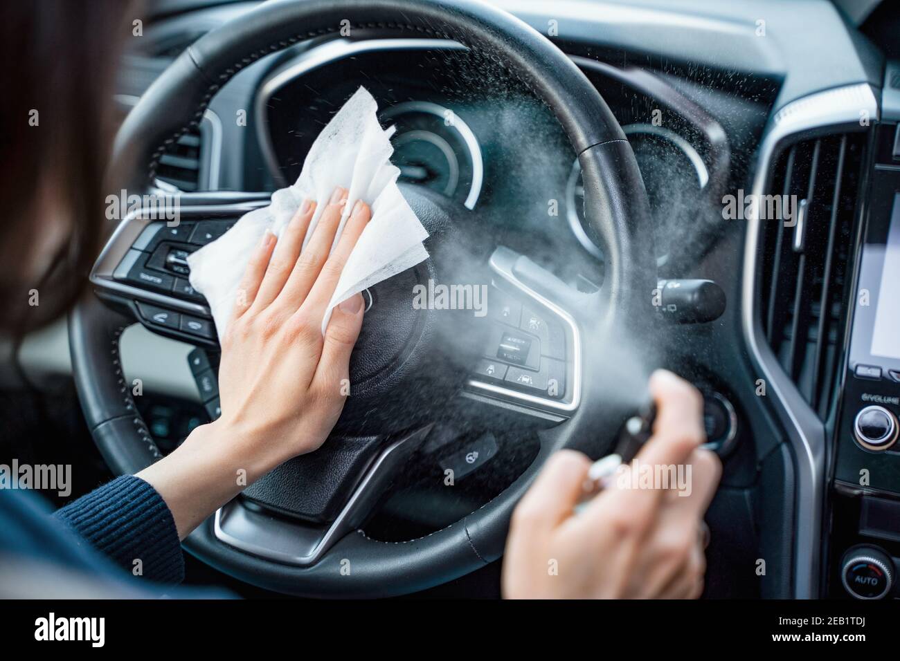 Mains de femme utilise un spray désinfectant sur le volant de direction vers l'intérieur sa voiture Banque D'Images