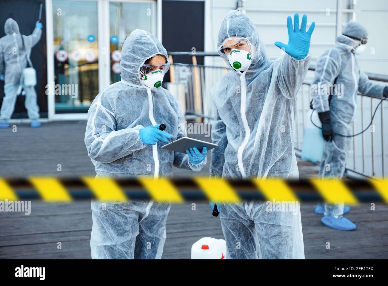 Professionnel de santé montrant un geste d'arrêt. Une équipe de professionnels de la santé portant des combinaisons de matières dangereuses travaille ensemble pour contrôler une épidémie dans la ville Banque D'Images