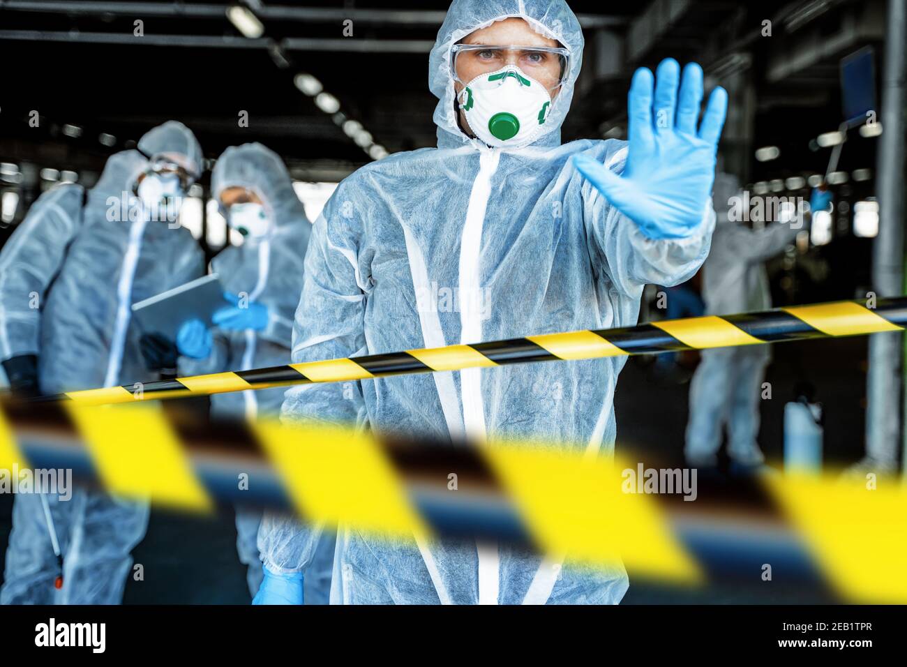 Professionnel de santé montrant un geste d'arrêt. Une équipe de professionnels de la santé portant des combinaisons de matières dangereuses travaille ensemble pour contrôler une épidémie dans la ville Banque D'Images