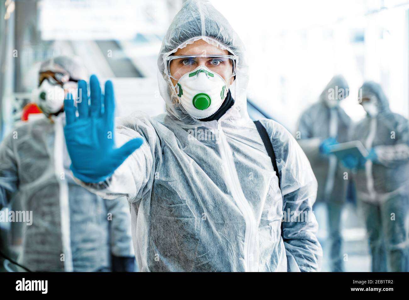 Professionnel de santé montrant un geste d'arrêt. Une équipe de professionnels de la santé portant des combinaisons de matières dangereuses travaillant ensemble dans un centre commercial, pour contrôler une épidémie de Banque D'Images