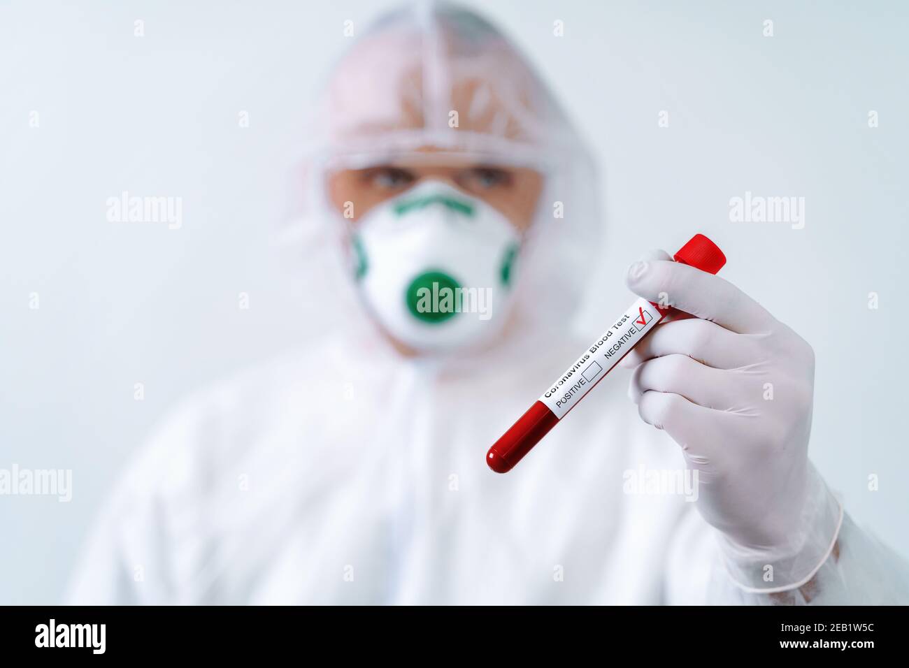 Test négatif COVID-19. Le virologue dans un masque médical et une combinaison de protection tient un tube à essai avec un échantillon de sang négatif Banque D'Images