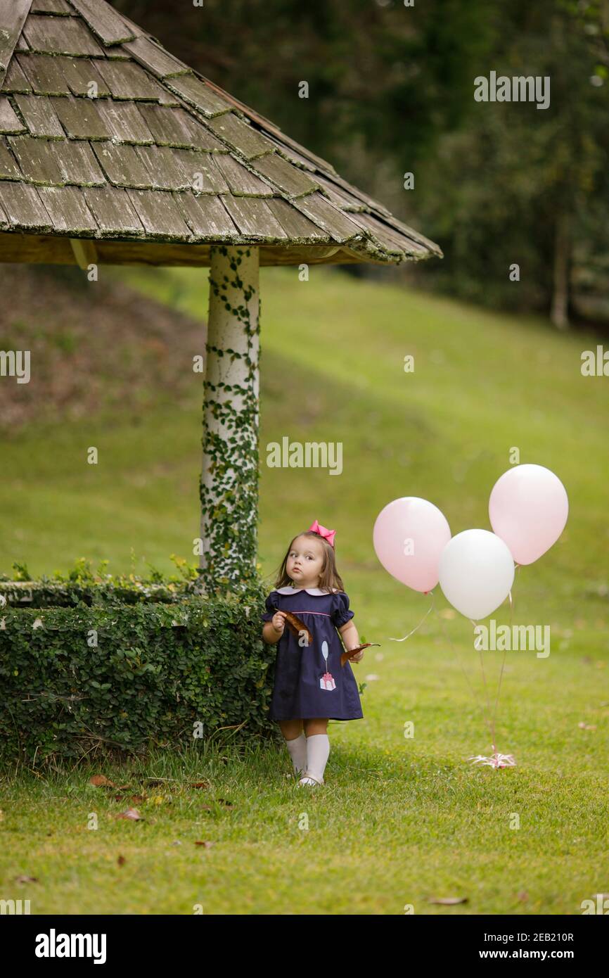 Petite fille avec ballons d'anniversaire roses marchant près d'un bonne chance à l'extérieur Banque D'Images