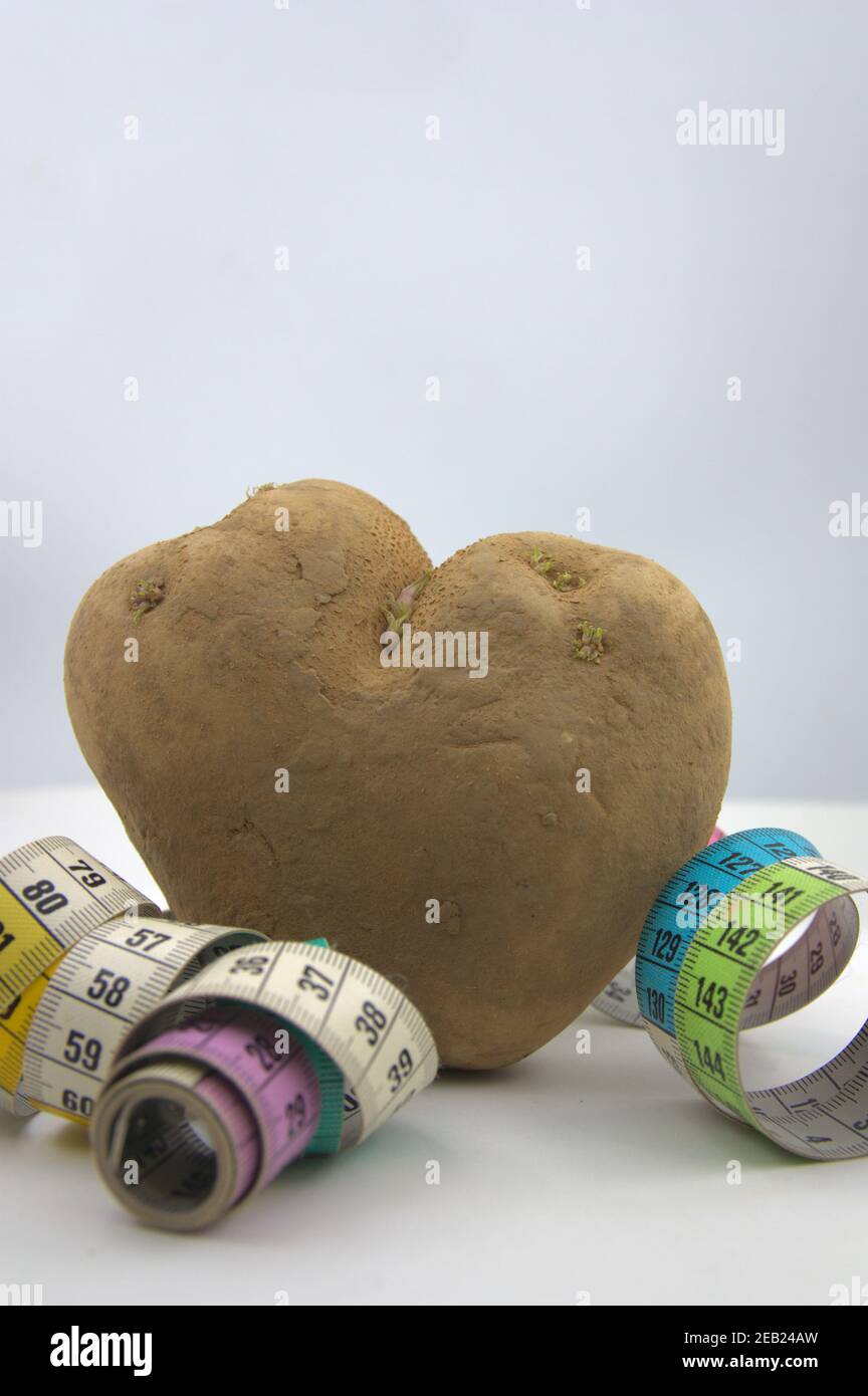 Image verticale dans laquelle une pomme de terre en forme de coeur avec un mesure de ruban autour de lui sur fond blanc et espace de copie Banque D'Images