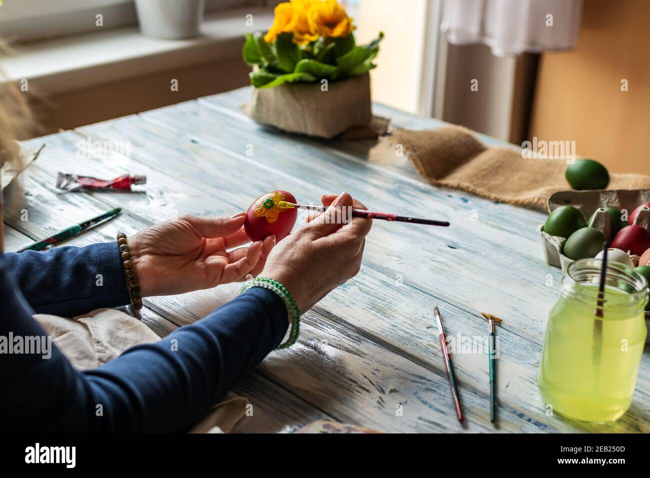 Femme peignant des œufs de Pâques traditionnels sur une table en bois. Préparer une décoration maison pour des vacances religieuses. Artisanat féminin créatif à la maison Banque D'Images