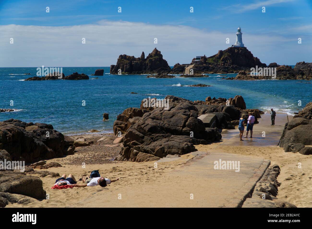 Les touristes vous détendre sur une portion de plage de sable fin avec la Corbiere Lighthouse en arrière-plan, Jersey, Channel Islands Banque D'Images