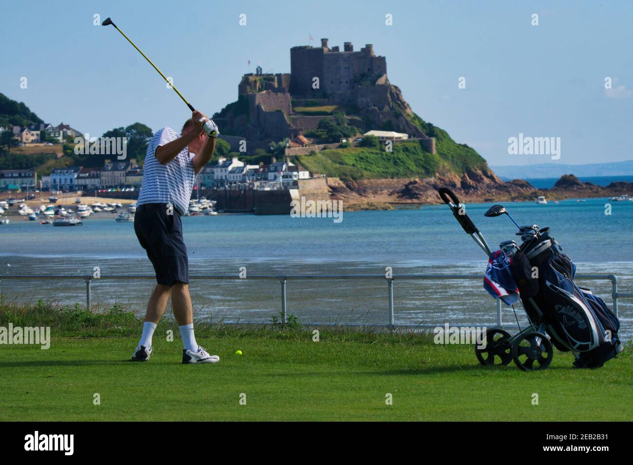 Un golfeur prend un coup à Gorey Castle dans le fond,Jersey,Channel Islands Banque D'Images