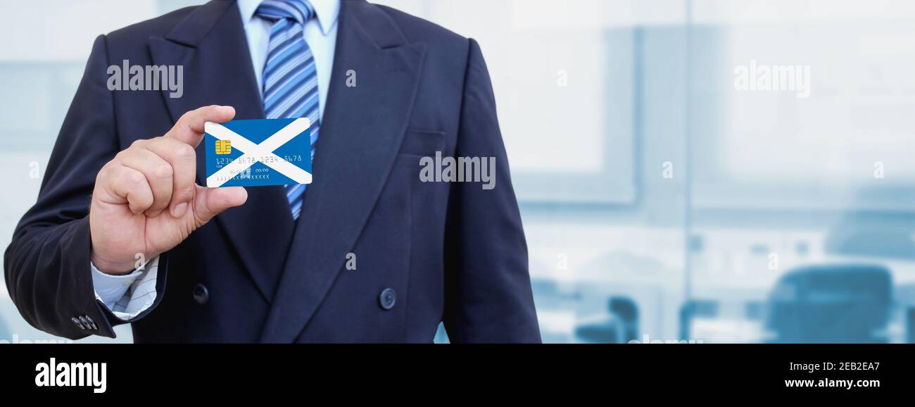 Image rognée d'un homme d'affaires tenant une carte de crédit en plastique avec drapeau imprimé de l'Écosse. Arrière-plan flou. Banque D'Images