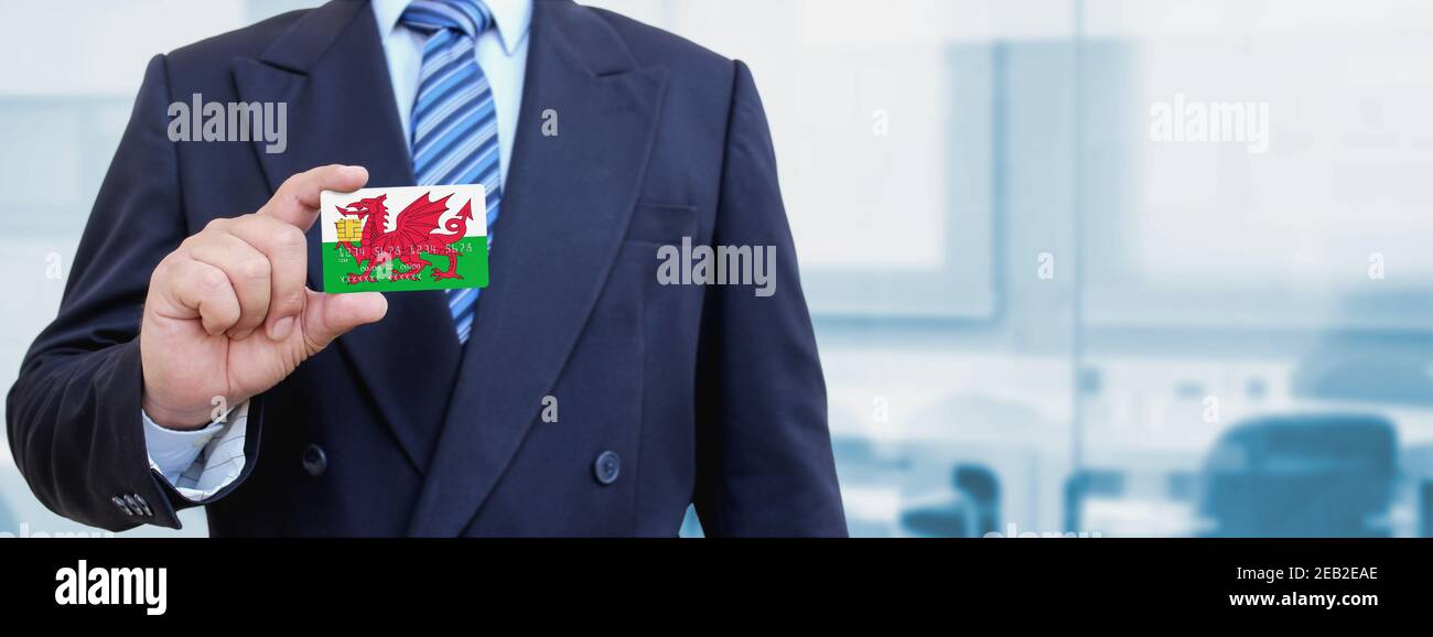 Image rognée d'un homme d'affaires muni d'une carte de crédit en plastique avec drapeau du pays de Galles imprimé. Arrière-plan flou. Banque D'Images