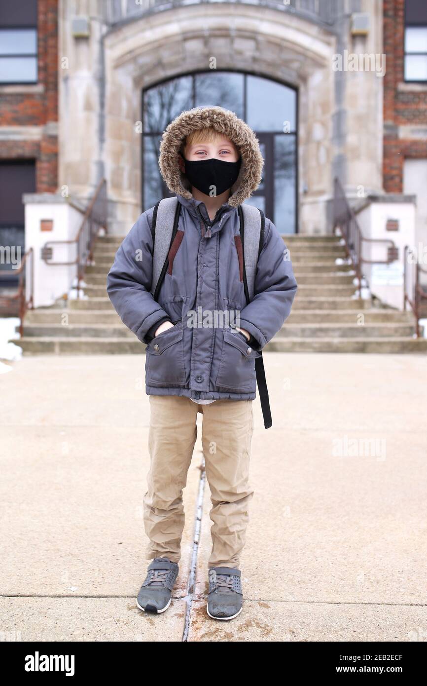 Un enfant de troisième catégorie portant un visage Covid protecteur masque est heureux de sourire comme il se tient à l'extérieur de son élémentaire bâtiment d'éducation scolaire pendant t Banque D'Images