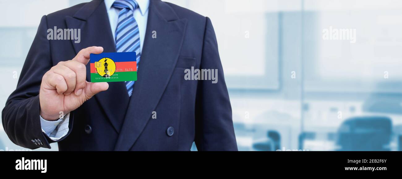 Image rognée d'un homme d'affaires muni d'une carte de crédit en plastique avec drapeau imprimé de la Nouvelle-Calédonie. Arrière-plan flou. Banque D'Images