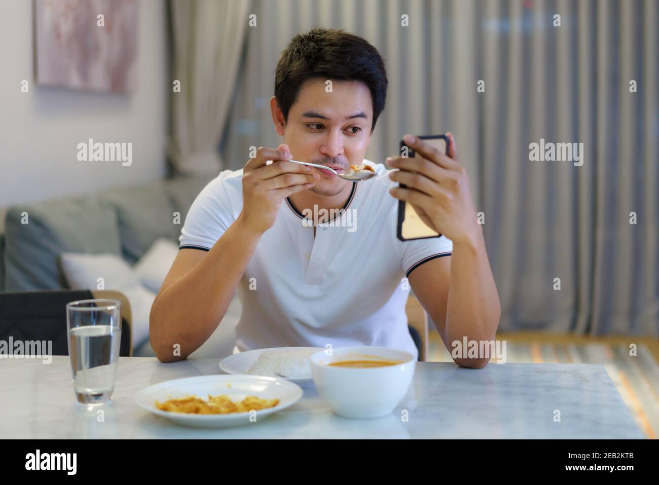 Un homme asiatique assis à la table du dîner et a eu un appel vidéo parlant à sa petite amie pour un dîner social distançant ensemble à la maison. Banque D'Images