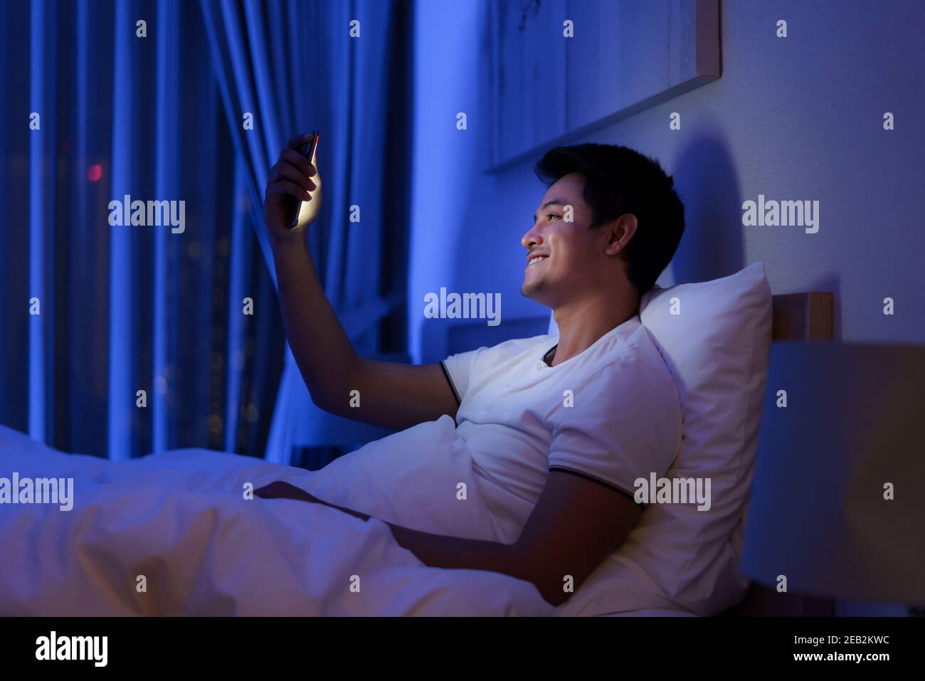 Homme asiatique virtuel happy hour réunion en ligne avec son petite amie dans la vidéo conférence à la bonne nuit avant de dormir à nuit avec un smartphone pour un Banque D'Images