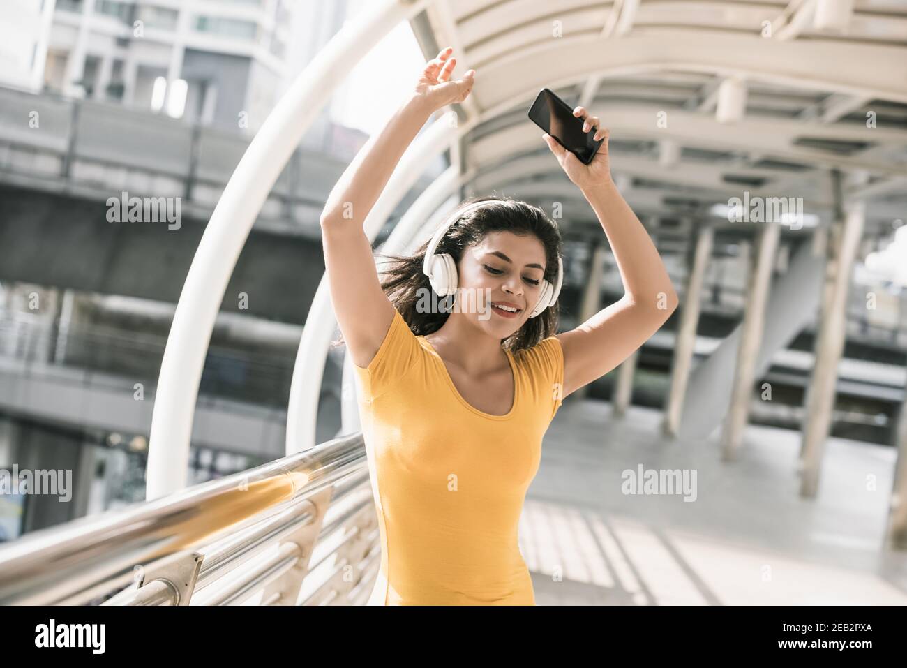 Bonne jeune femme Latino à l'écoute de la musique des écouteurs et dansez avec les mains dans la passerelle couverte de la ville Banque D'Images