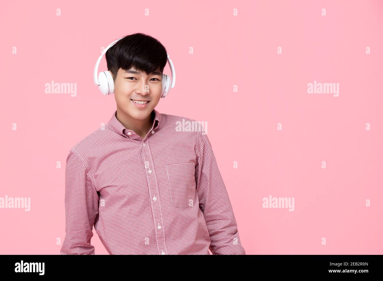 Beau homme asiatique souriant portant un casque à l'écoute de studio de musique photo isolée sur fond rose Banque D'Images