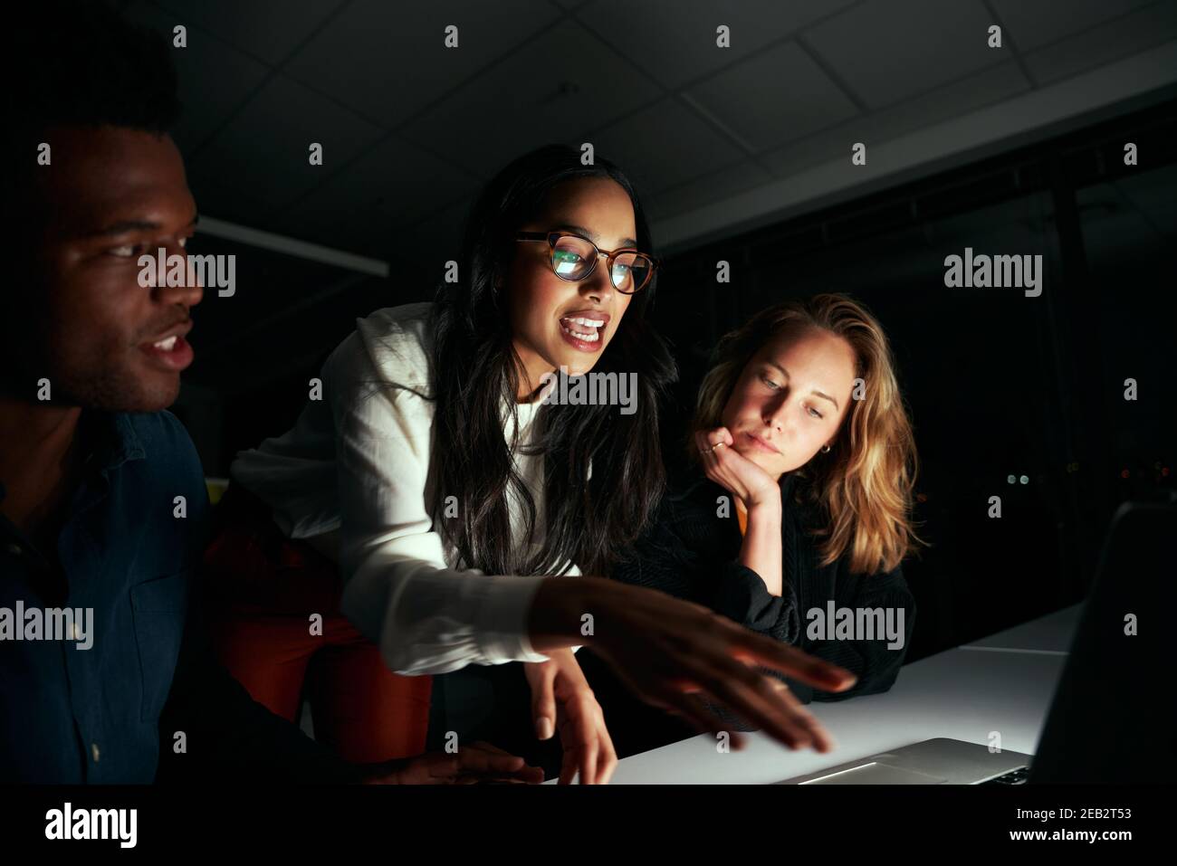Jeune femme d'affaires discutant du projet avec ses deux collègues dans le bureau sombre jusqu'à tard dans la nuit Banque D'Images
