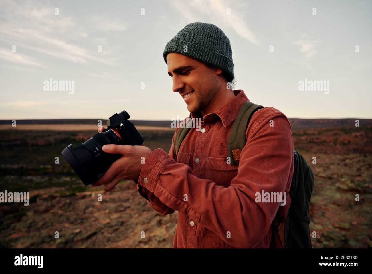 Un photographe de voyage masculin vérifie les photos sur l'appareil photo après avoir pris une photo debout sur la montagne, le bonnet et le sac à dos Banque D'Images