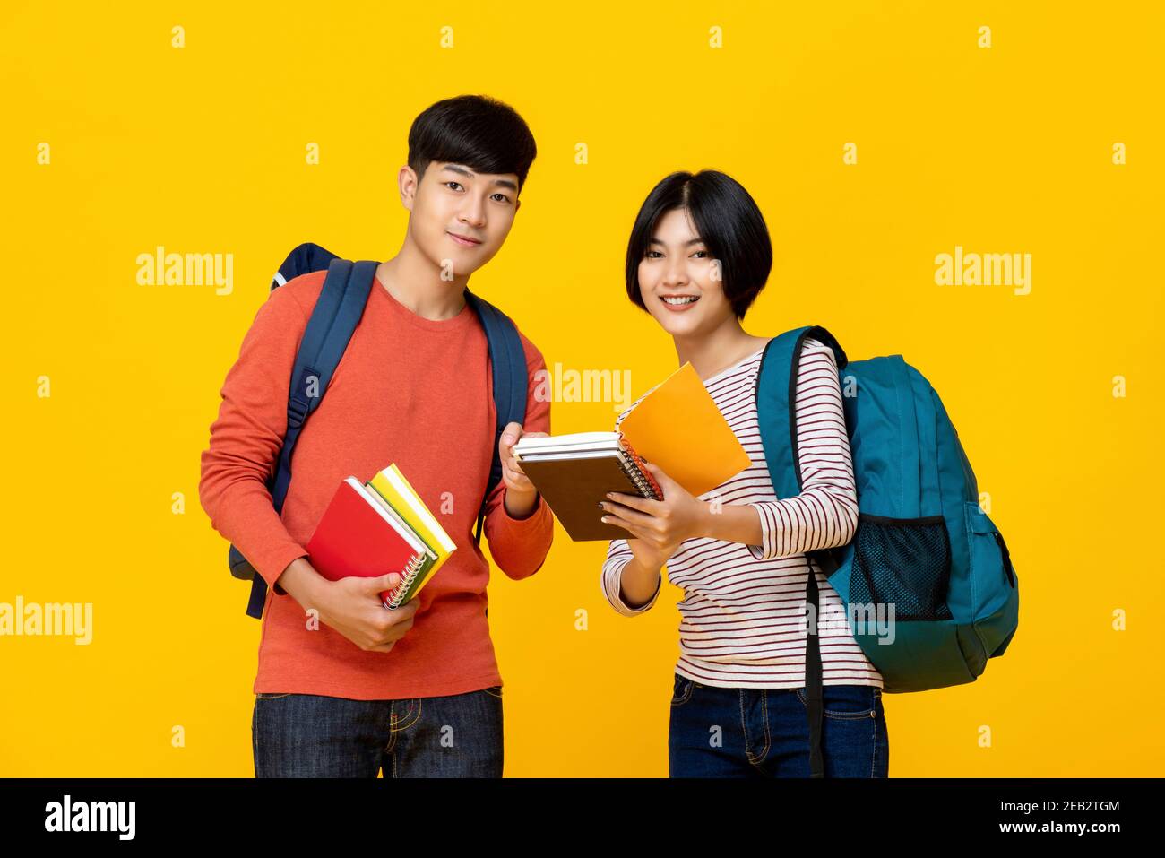 Des amis asiatiques souriants, hommes et femmes, étudiants à l'université avec des sacs à dos tenue de livres sur fond de studio jaune coloré Banque D'Images