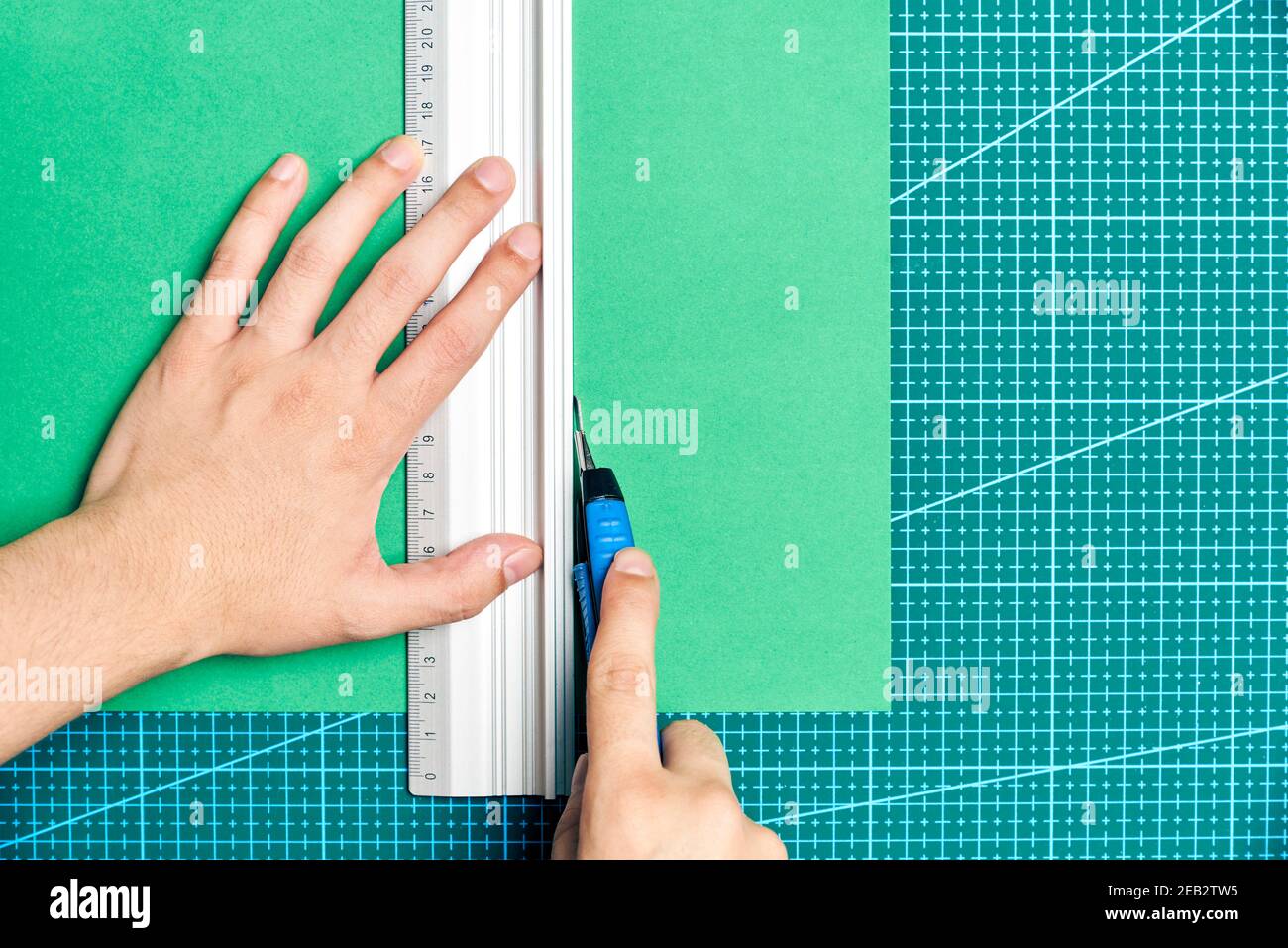 Les jeunes femmes coupent une feuille de papier verte avec un couteau et une règle métallique sur une planche à découper. Image de mise en page à plat avec espace de copie. Banque D'Images