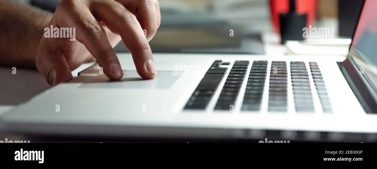 Doigts d'un homme travaillant sur ordinateur portable pavé tactile la nuit, bannière proportion sélective focus Banque D'Images