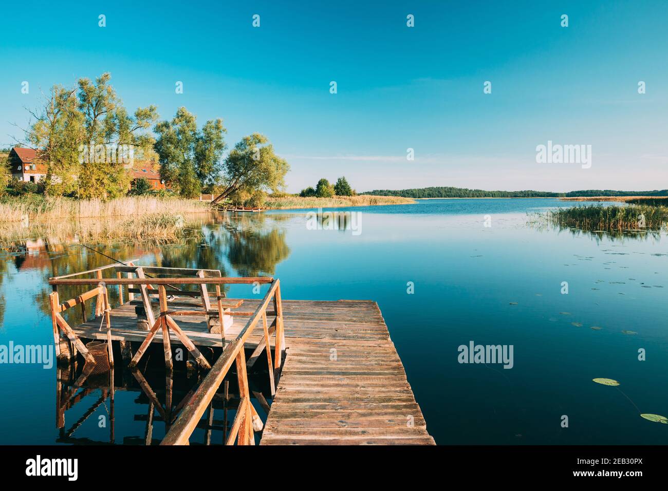 Ancienne jetée de pêche en bois près du lac d'été ou de la rivière. Eau calme dans la belle journée ensoleillée d'été. Banque D'Images