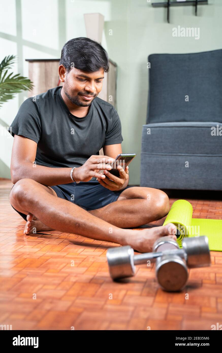 Jeune homme occupé à utiliser le téléphone portable pendant l'exercice - Tutoriels d'exercice en ligne de vérification millénaire pour l'entraînement - concept de salle de gym à la maison en raison du coronavirus Banque D'Images