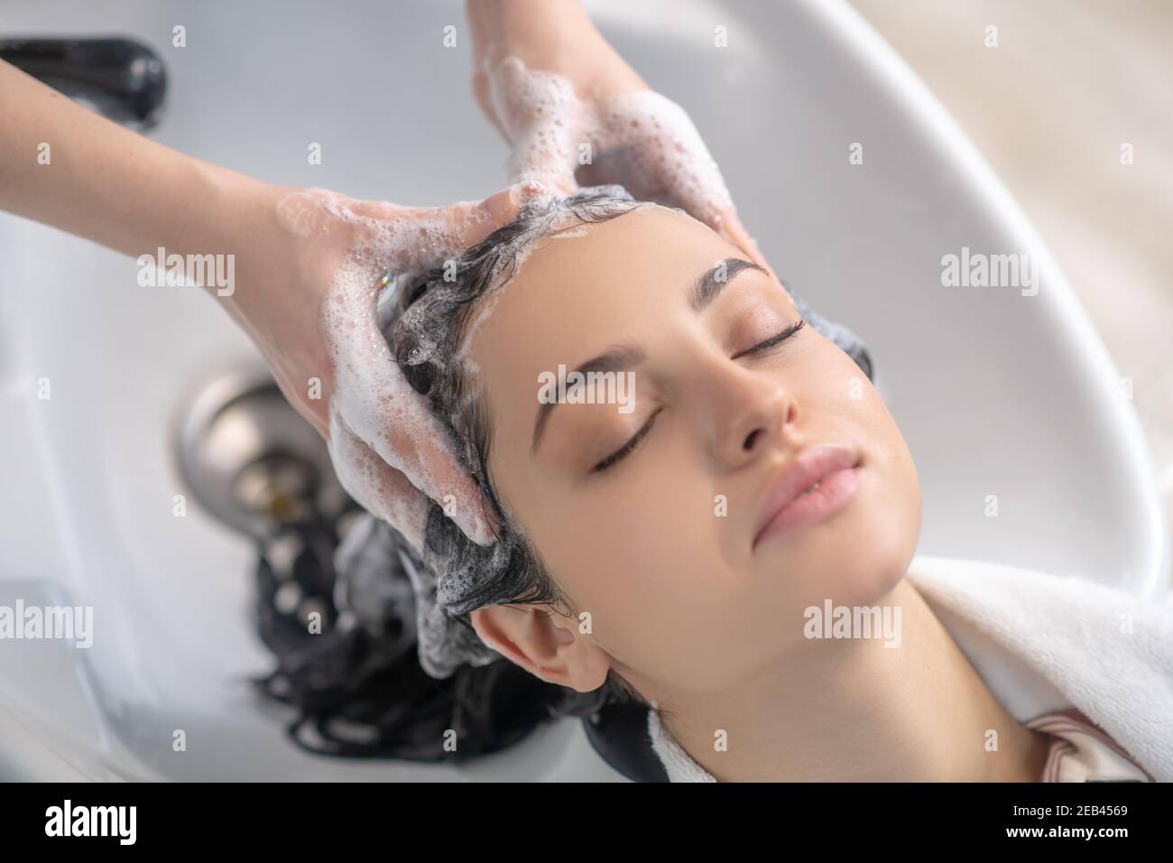Elle a l'air détendue tandis que la coiffeuse lavant ses cheveux avec shampooing Banque D'Images
