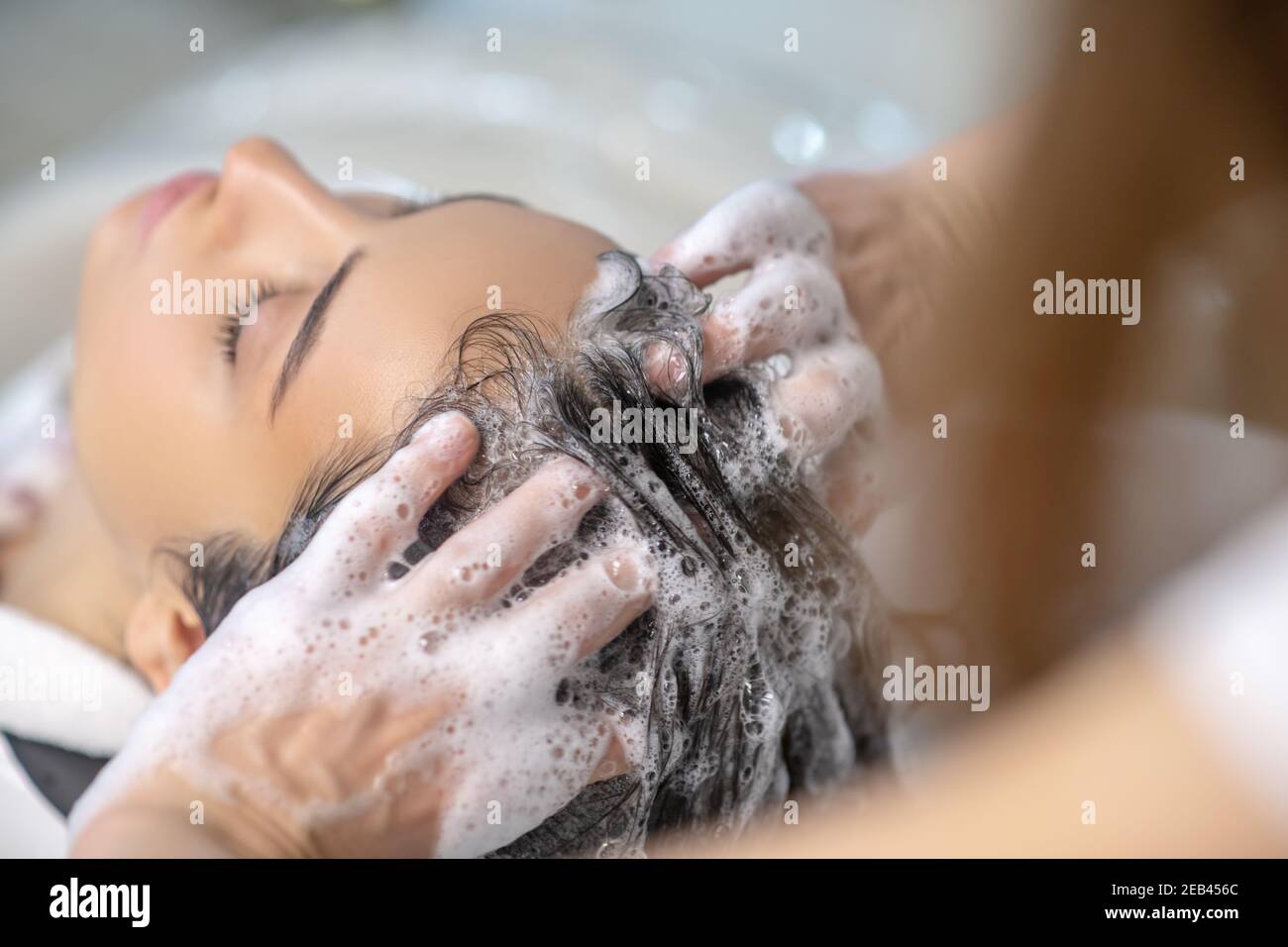 Elle a l'air détendue tandis que la coiffeuse lavant ses cheveux avec shampooing Banque D'Images