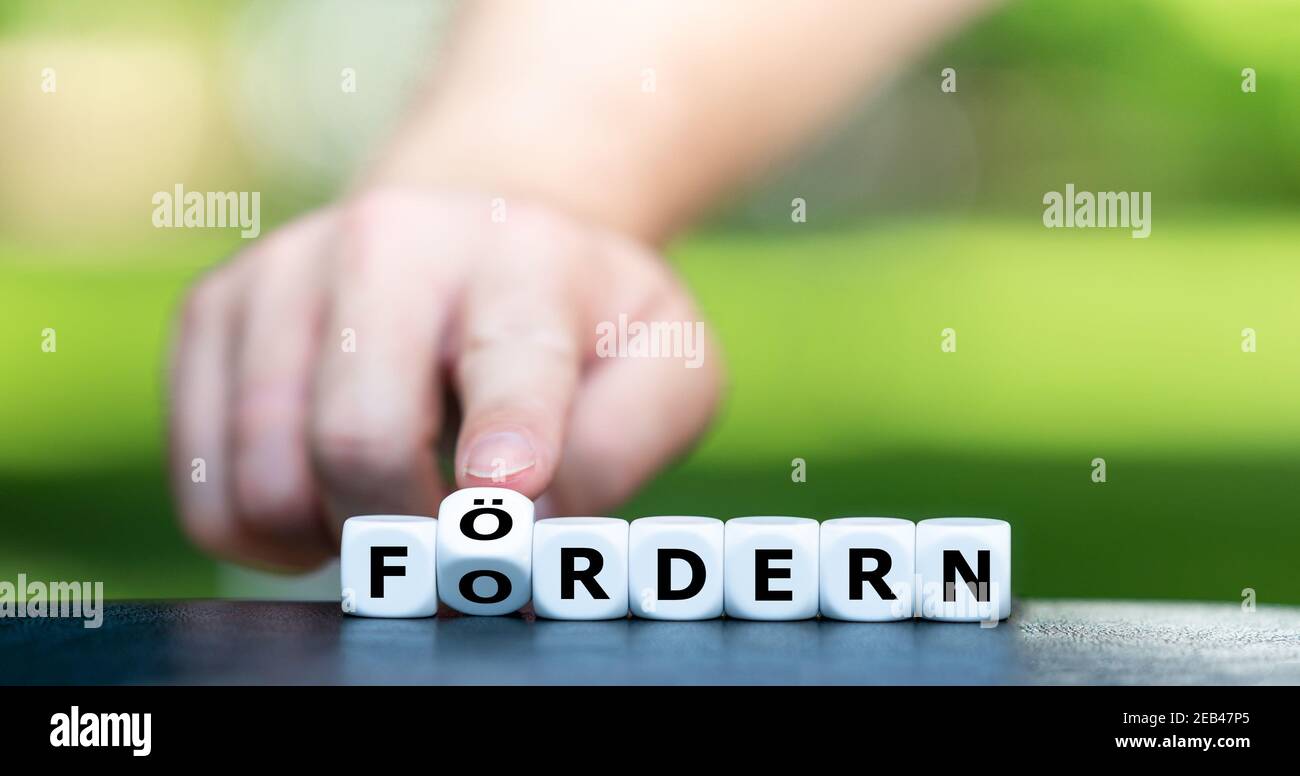 La main tourne les dés et change l'expression allemande 'fordern' (demande) en 'foerdern' (support). Banque D'Images