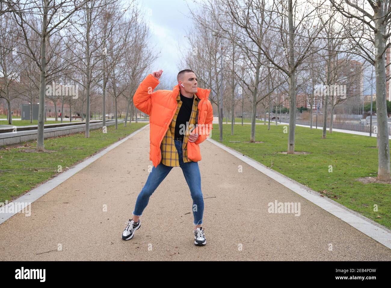 Beau jeune homme portant du maquillage et des écouteurs, dansant sur un sentier de parc. Type androgyne non binaire. Banque D'Images