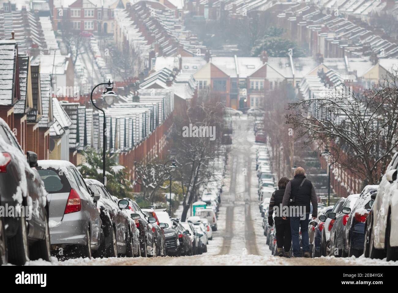 Un couple qui descend de la colline dans le quartier de Crouch End, Londres avec une toile de fond de maisons en terrasse couvertes de neige Banque D'Images