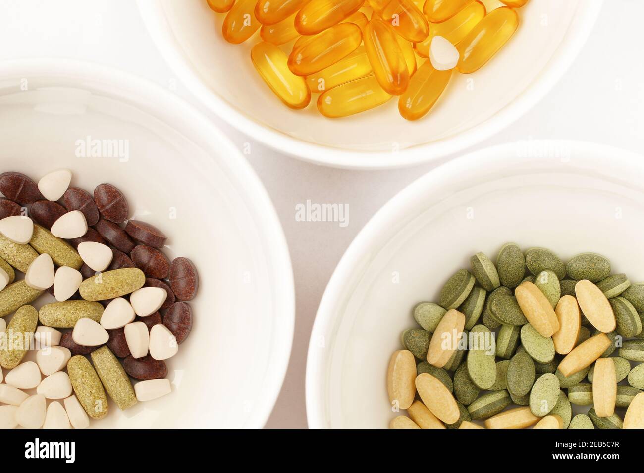 Trois bols avec vitamines, suppléments alimentaires et capsules d'huile de poisson sur fond blanc, vitamine omega, capsules jaunes transparentes Banque D'Images