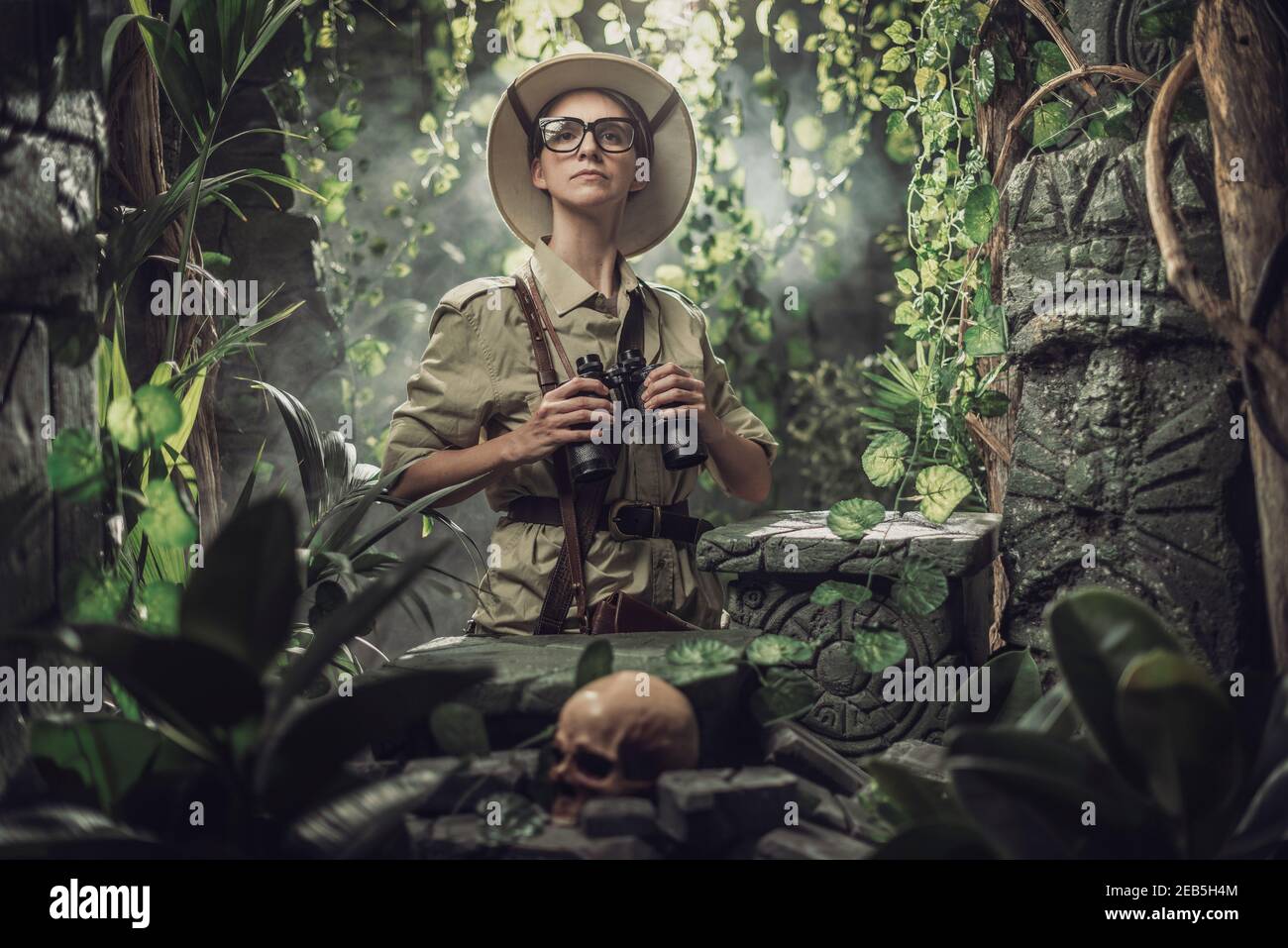 Femme courageuse explorant la jungle tropicale et trouvant des ruines antiques, elle tient des jumelles et regarde autour Banque D'Images