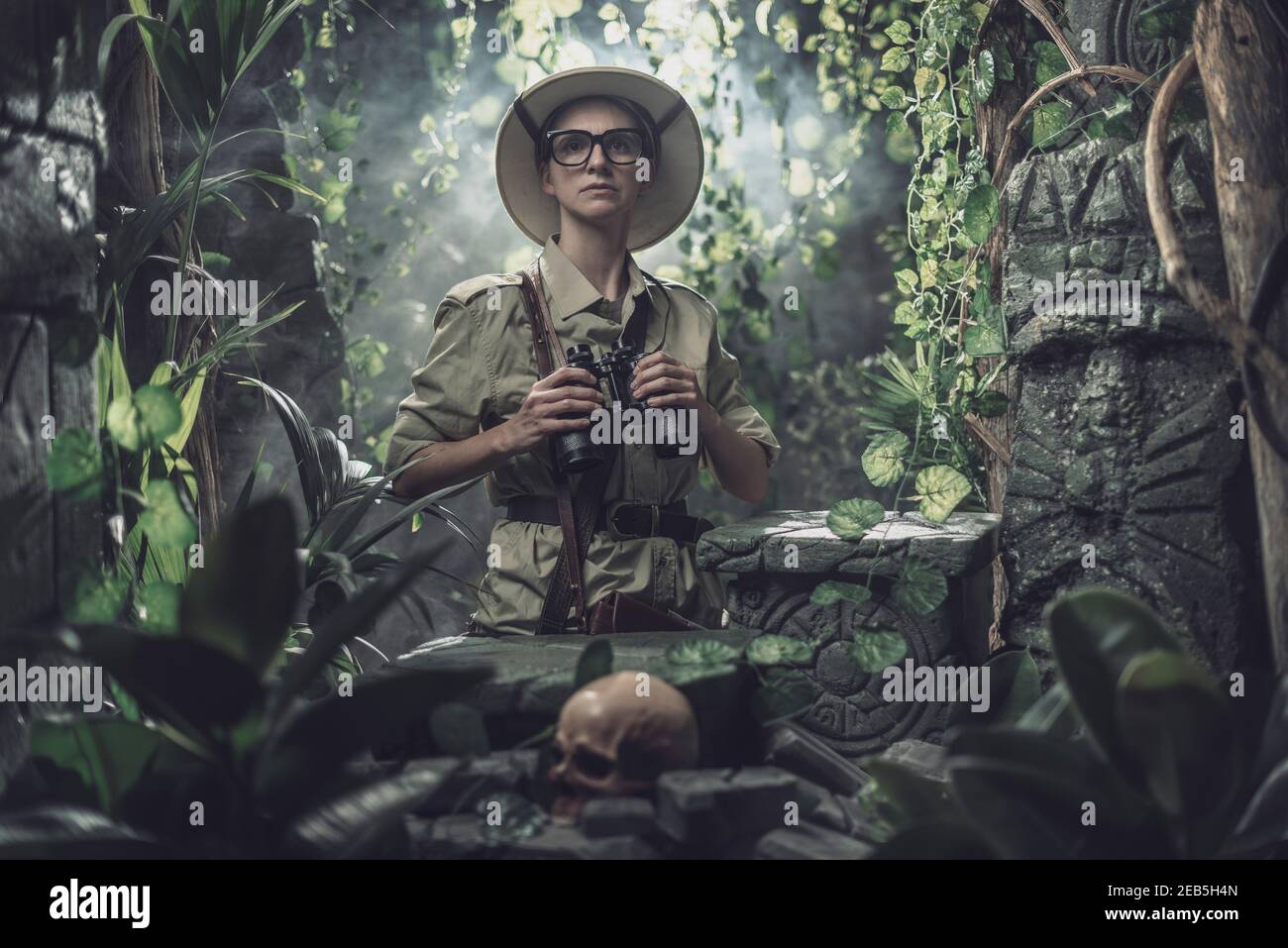 Femme courageuse explorant la jungle tropicale et trouvant des ruines antiques, elle tient des jumelles et regarde autour Banque D'Images
