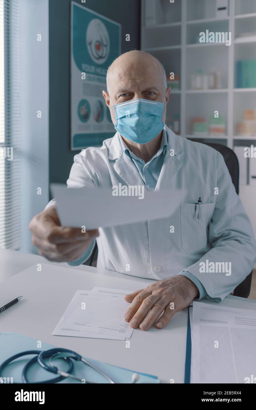 Médecin dans son bureau donnant une ordonnance au patient, il porte un masque chirurgical protecteur, point de vue Banque D'Images