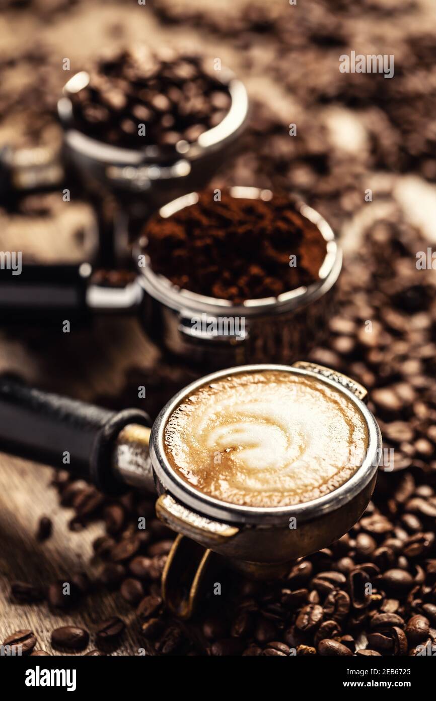 Le café sous ses différentes formes, des grains de café crus au café moulu et au cappuccino dans trois portafiltres. Banque D'Images