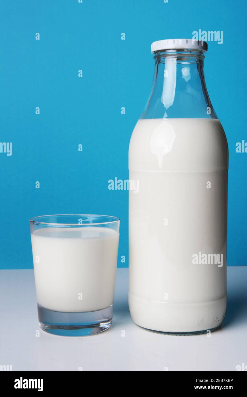 Bouteille en verre de lait frais avec son plein verre pour un bon petit déjeuner. Photo isolée sur fond bleu avec ombre Banque D'Images