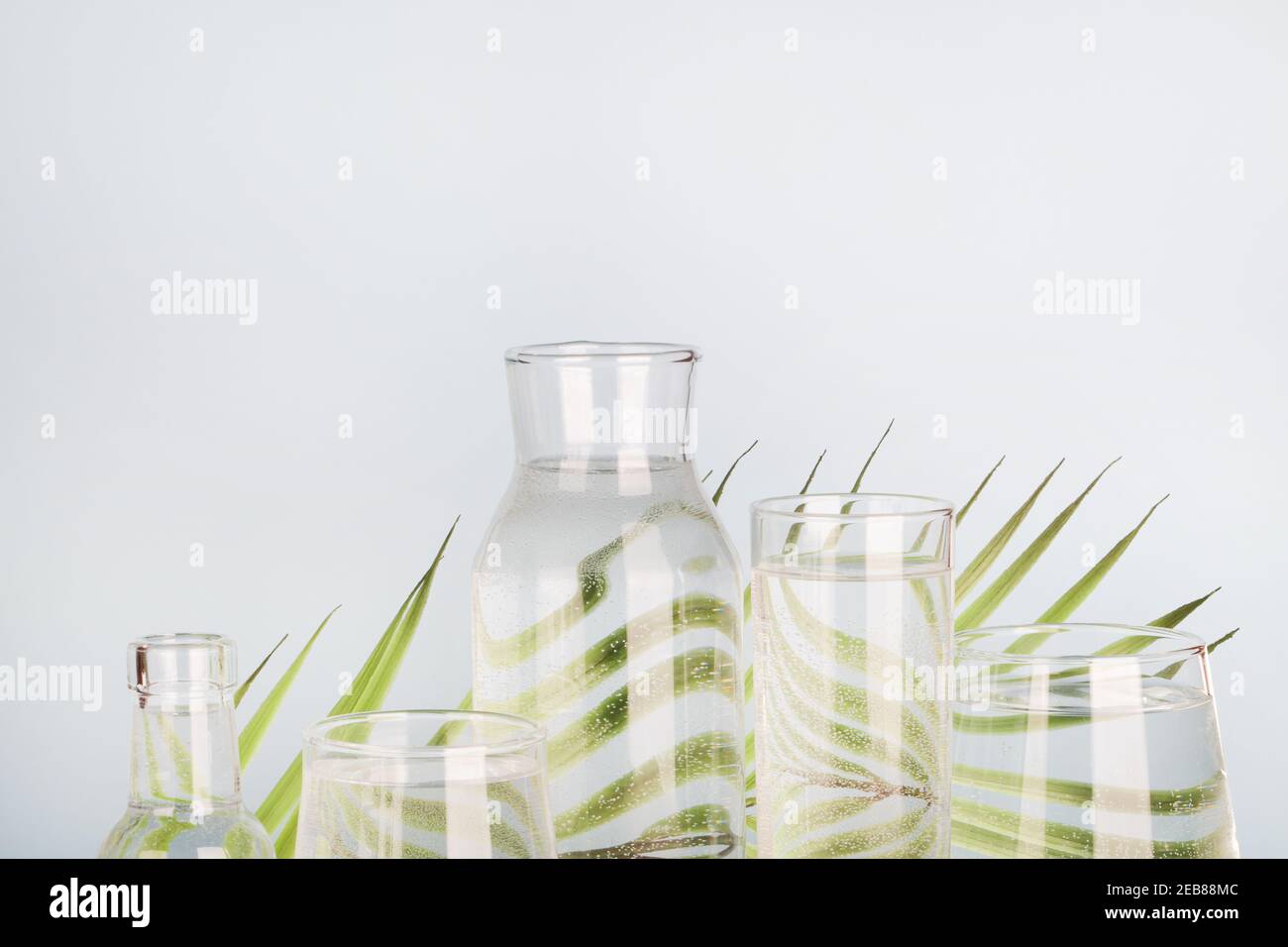 feuille de palmier déformée dans l'eau dans les verres et les bouteilles sur fond bleu. Décoration maison, écologique, eau pure, concept de jardinage.espace de copie Banque D'Images