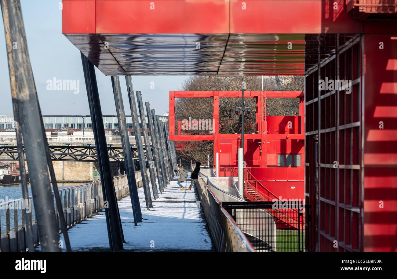 Les touristes prenant des photos sur la porte enneigée du Parc de la Villette à Paris 19ème passant sous des structures de métal rouge vif appelées 'folies'. Banque D'Images