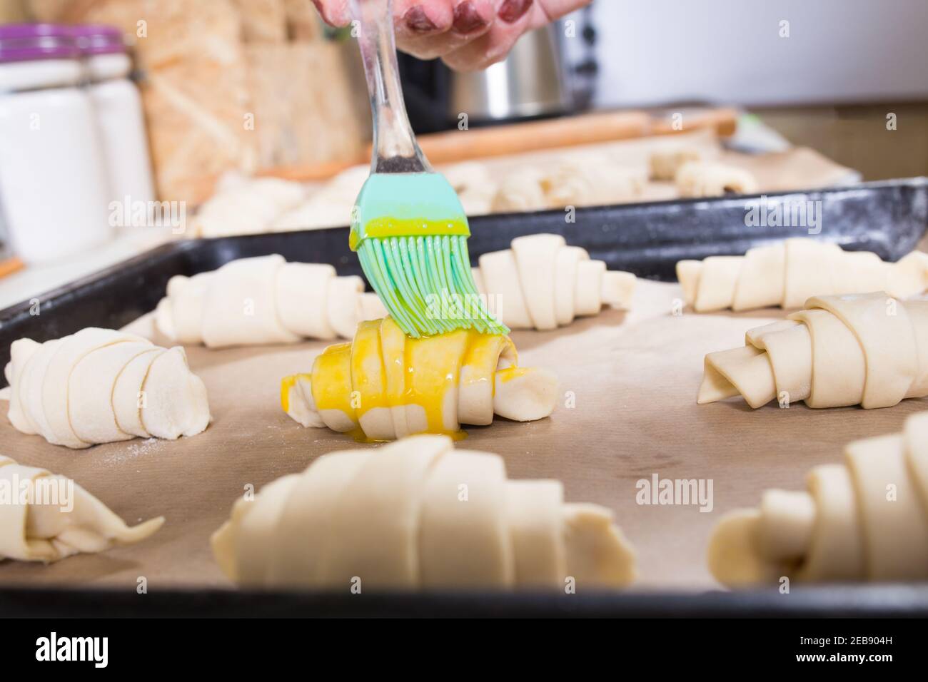 HAMD brossant des croissants crus avec une brosse à pâtisserie, sur une plaque métallique avec du papier de cuisson. Banque D'Images