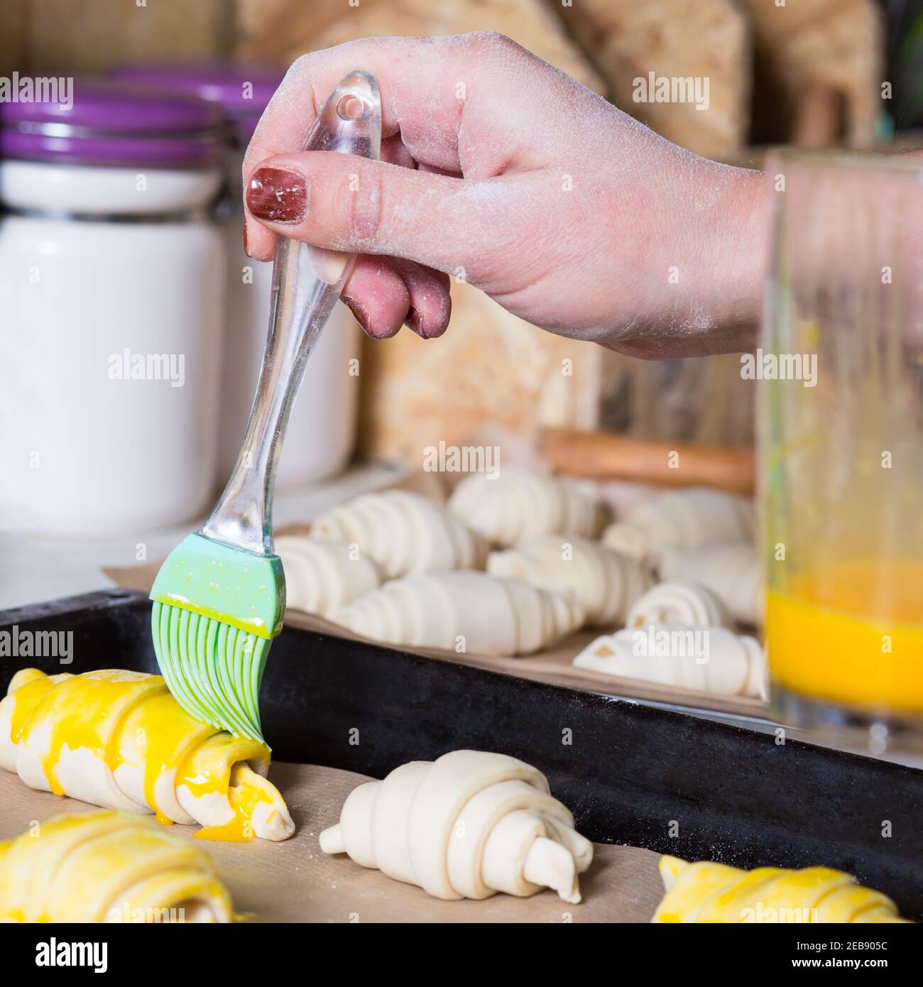 Utilisez une brosse à pâtisserie pour brosser les croissants crus, sur une plaque métallique avec du papier de cuisson. Banque D'Images