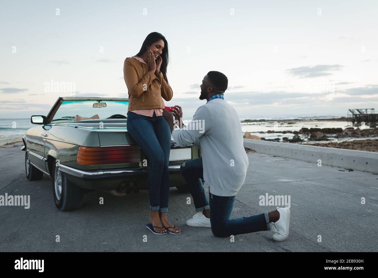 Divers couple debout par un homme de voiture décapotable propose à femme Banque D'Images