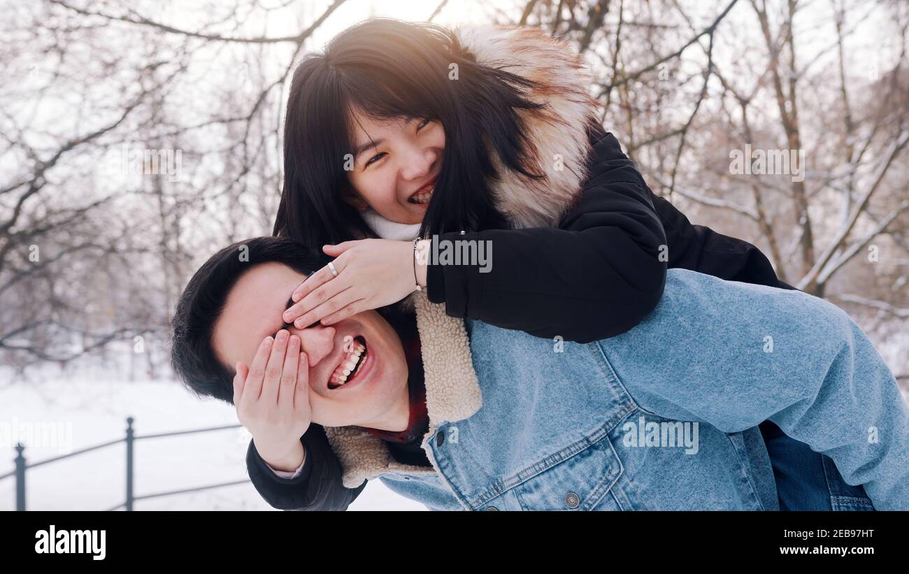 Un jeune homme donne un pigeyback à sa petite amie dans le parc le jour d'hiver enneigé. Un couple asiatique neuf s'est amusé dehors. Photo de haute qualité Banque D'Images