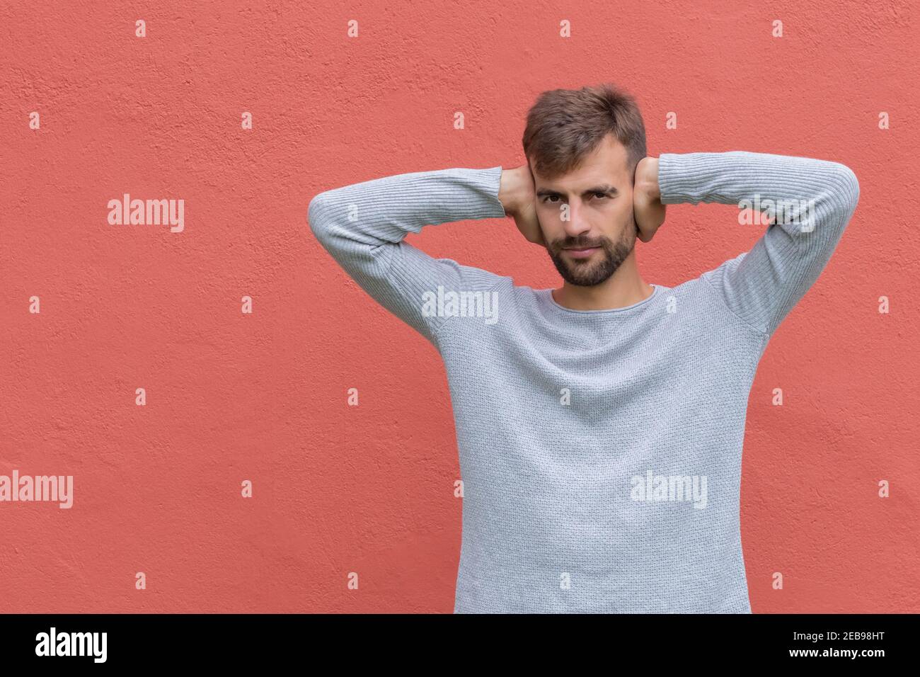 Homme barbu couvrant les oreilles en ignorant le bruit. Un gars stressé se bouchant les oreilles avec les paumes. Mâle couvrant les oreilles en raison de douleurs à la tête. Un homme frustré se ferme les oreilles Banque D'Images
