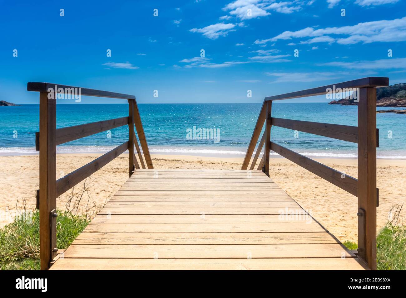 Promenade jusqu'à la plage de sable. Passerelle en bois au-dessus du sable vers la mer. Plage ensoleillée avec plancher de promenade en bois. Arrière-plan des vacances. Concept de vacances d'été. Copier la flèche Banque D'Images