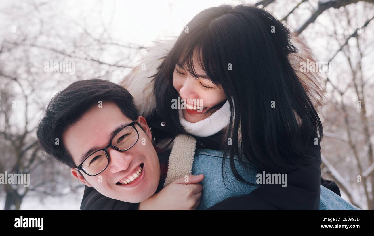 Un jeune homme donne un pigeyback à sa petite amie dans le parc le jour d'hiver enneigé. Un couple asiatique neuf s'est amusé dehors. Photo de haute qualité Banque D'Images