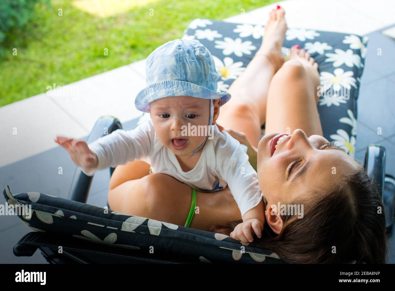 Jolie maman aimante essayant d'apaiser le bébé rouge cramoisi et de se débarrasser de la peur de bébé en la tenant dans les bras de mère, en embrassant et en souriant avec joie Banque D'Images