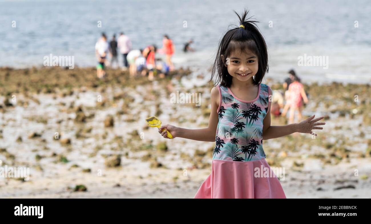 Bonne petite fille sur la plage tenant un jouet de plage et un maillot de bain coloré. Banque D'Images