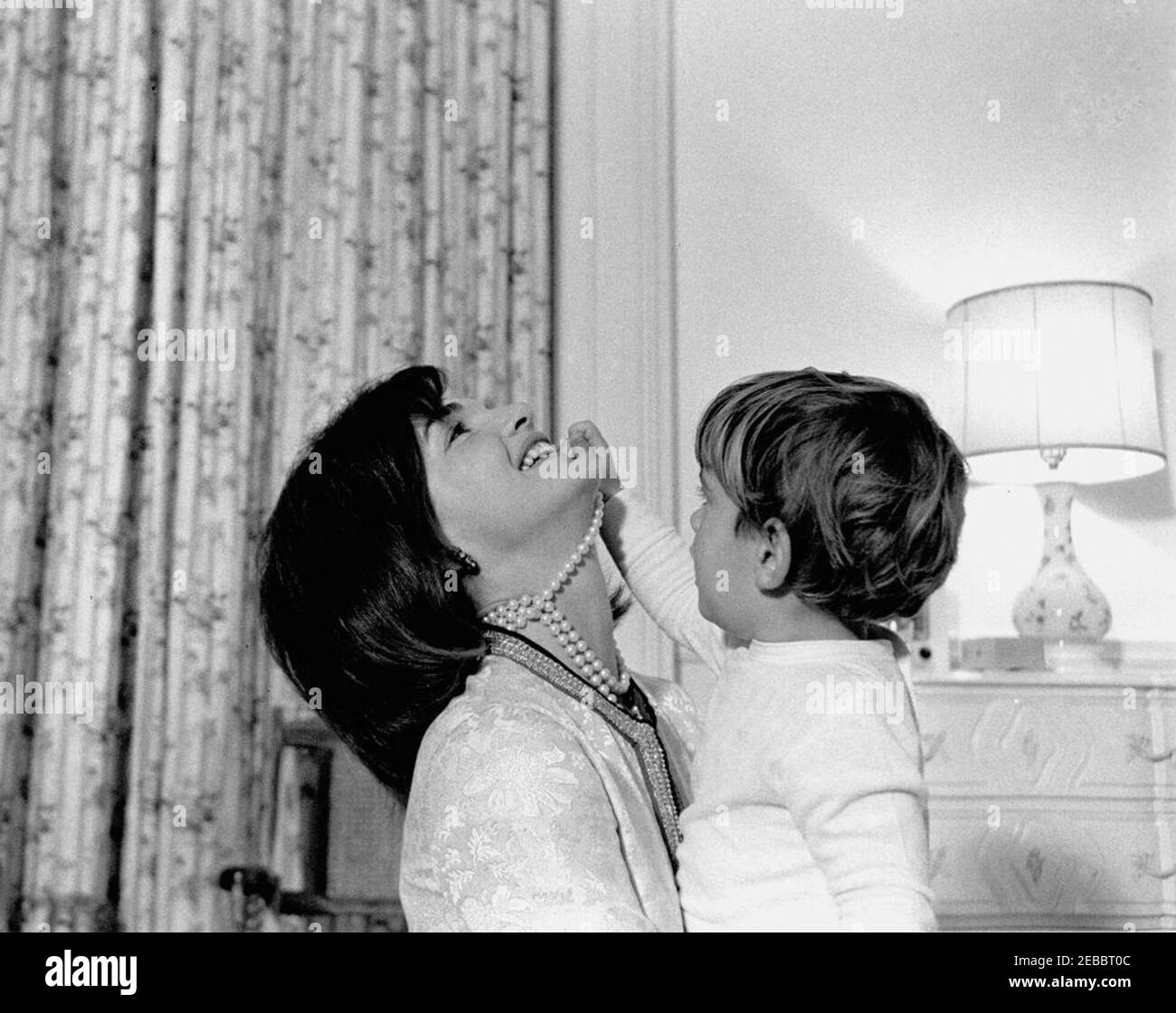Le président Kennedy, la première dame Jacqueline Kennedy (JBK) et les enfants de la pépinière de la Maison Blanche. La première dame Jacqueline Kennedy rit tandis que son fils, John F. Kennedy, Jr., joue avec son collier de perles simulées dans la pépinière de Johnu2019s, après une fête d'anniversaire conjointe pour lui et sa sœur, Caroline Kennedy. White House, Washington, D.C. Banque D'Images Le président Kennedy, la première dame Jacqueline Kennedy (JBK) et les enfants de la pépinière de la Maison Blanche. La première dame Jacqueline Kennedy rit tandis que son fils, John F. Kennedy, Jr., joue avec son collier de perles simulées dans la pépinière de Johnu2019s, après une fête d'anniversaire conjointe pour lui et sa sœur, Caroline Kennedy. White House, Washington, D.C. Banque D'Images