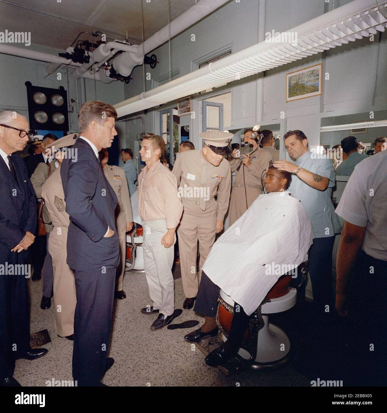 Voyage dans les États de l'Ouest : San Diego, Californie, Marine corps Recruit Depot, visite des casernes, inspection des recrues et adresse à Hall Field. Le président John F. Kennedy (à gauche) et le commandant du régiment de formation des recrues du Marine corps Recruit Depot (MCRD), le colonel Merrill M. Day (au centre), observent alors qu'une recrue reçoit une coupe de cheveux dans le salon de coiffure du MCRD à San Diego, en Californie. Également en photo : le secrétaire de la Marine, Fred Korth; l'aide navale au président, le capitaine Tazewell T. Shepard, Jr.; l'agent du service secret de la Maison Blanche, Gerald A. u0022Jerryu0022 Behn. Banque D'Images